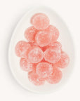 On a white background is a white egg shaped dish with round light pink candies dusted with white sugar.