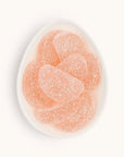 Half moon shaped grapefruit gummy slices covered in shimmering sugar crystals. The blush pink gummies are placed in a small white bowl.