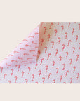 A single sheet of gift wrap with a blush background and a repeating red and white candy cane print. The gift wrap is reversible and the other side features a light purple / lavender background with an all over red and white candy cane design but the candy canes are slightly smaller than the reverse.