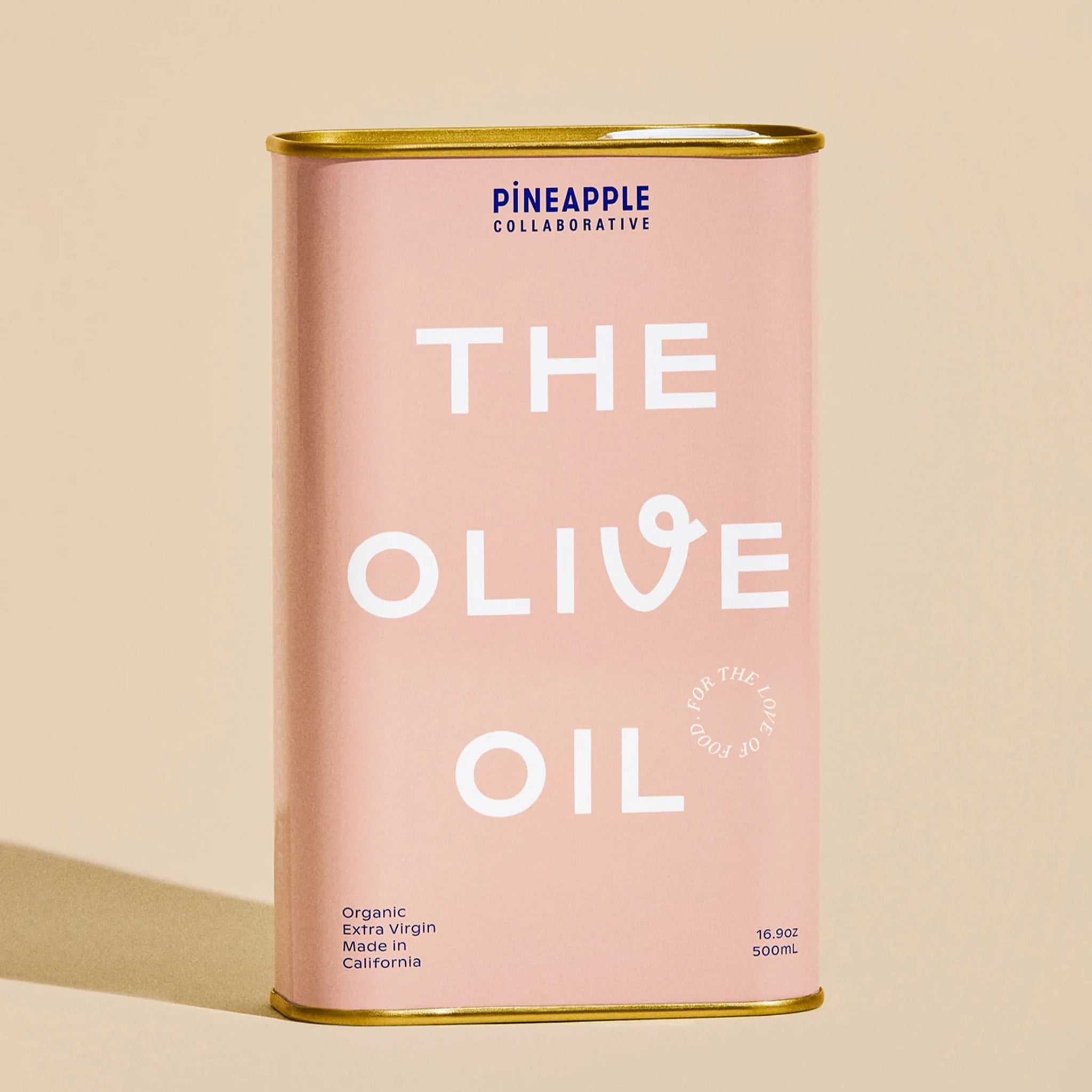 A pink tin of olive oil with gold accents on the top and bottom along with white text that reads, &quot;The Olive Oil&quot;.