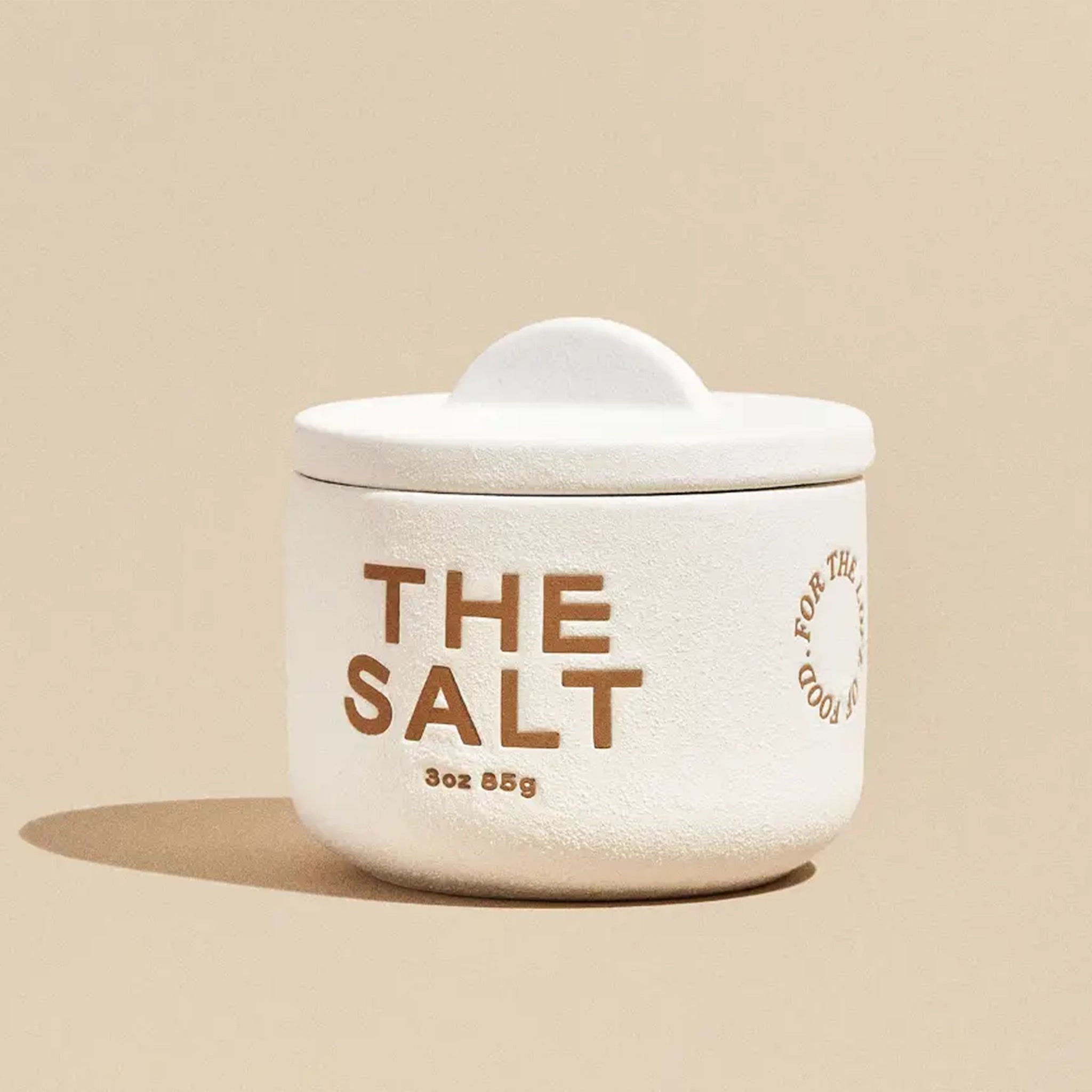 A 3oz bespoke pinch pot with a half moon lid that marries form and function along with brown text on the front that reads, "The Salt 3oz 85g".