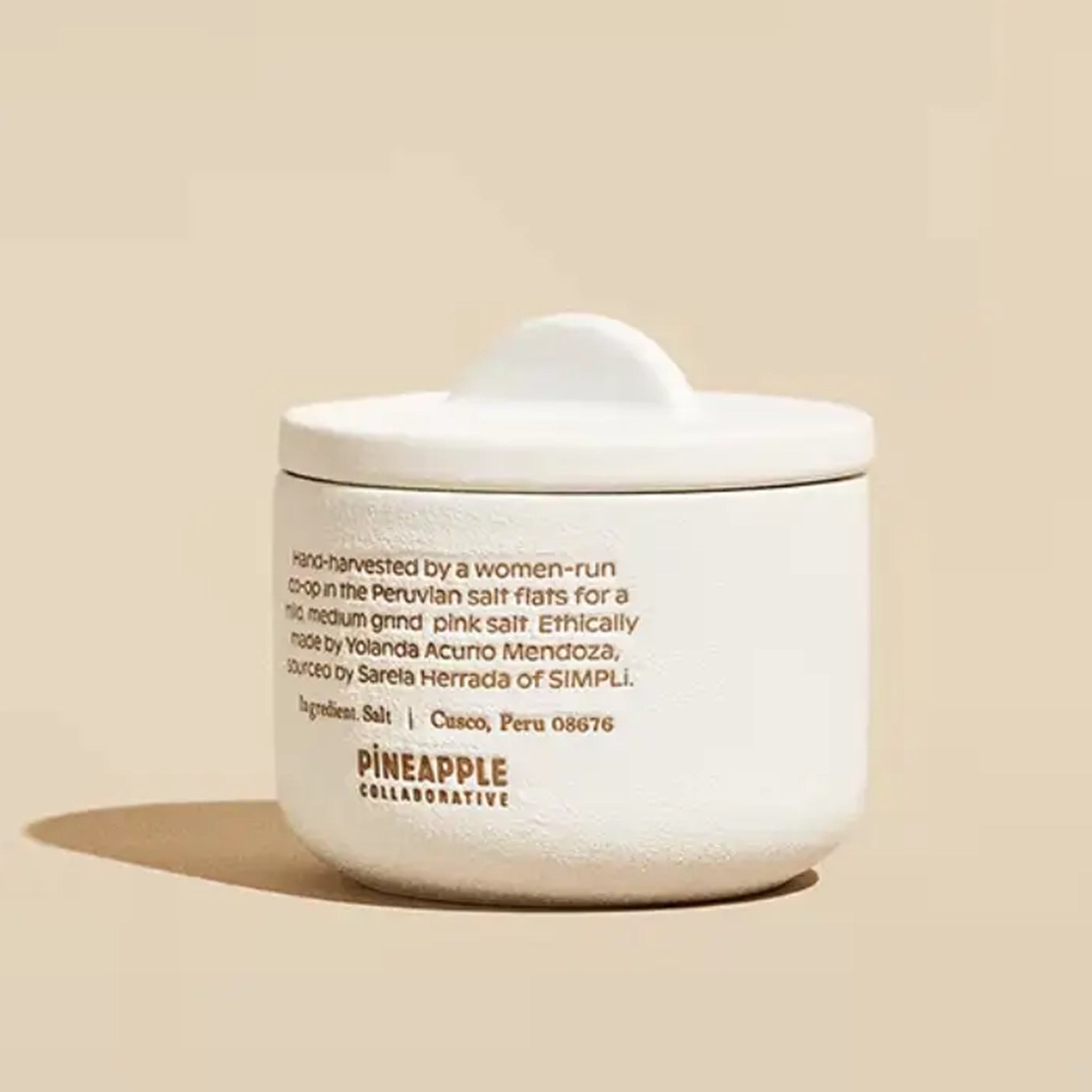 The back of the white ceramic pinch pot that reads, &quot;Hand-harvested by a women-run co-op int he Peruvian salt flats for a mild medium grind pink salt. Ethically made by Yolanda Curio Mendoza, sourced by Sara Herrada of SIMPLi.&quot;.