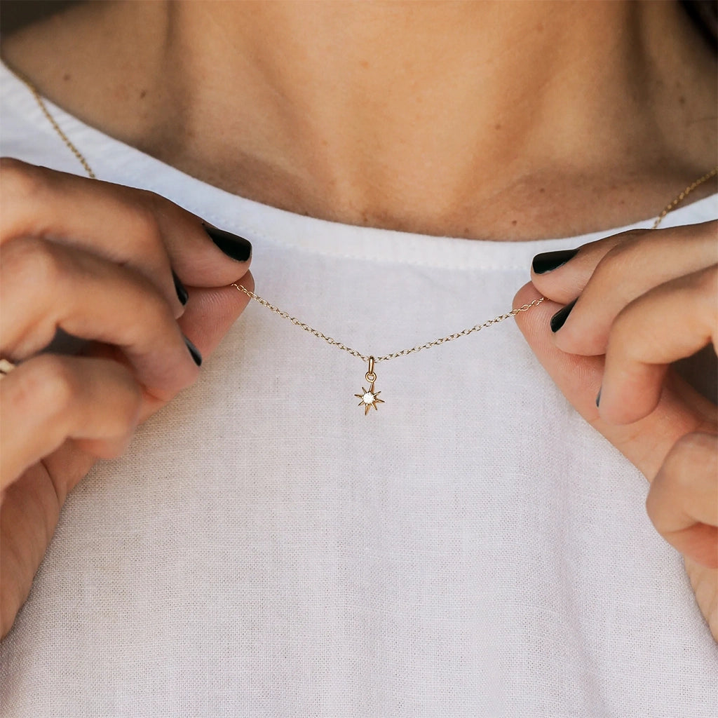 A gold chain necklace with a tiny eight pointed star charm along with a single CZ stone in the center.