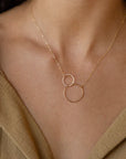 A model wearing the unity necklace features two gold circles, hand forged and lightly hammered that come together and hang from a beautiful chain.