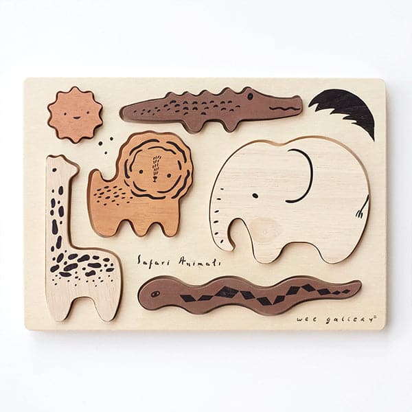 6 wooden puzzle pieces shaped as African animals including a beech wood elephant and giraffe, teak colored lion and chocolate crocodile and snake. All pieces are positioned within the ivory puzzle tray labeled 'Safari Animals' in delicate black lettering found towards the bottom half of the puzzle. The puzzle lays against a solid white background.