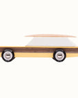 This wooden station wagon model has an elongated daffodil yellow body with walnut veneer-paneled sides, providing the ultimate classic feel. Wheels are jet black reading 'Candylab Mo-To' around white and silver rims. The windowed top half consists of a single white trapezoid shaped wooden block. A magnetic beech wood surfboard lays directly on top.