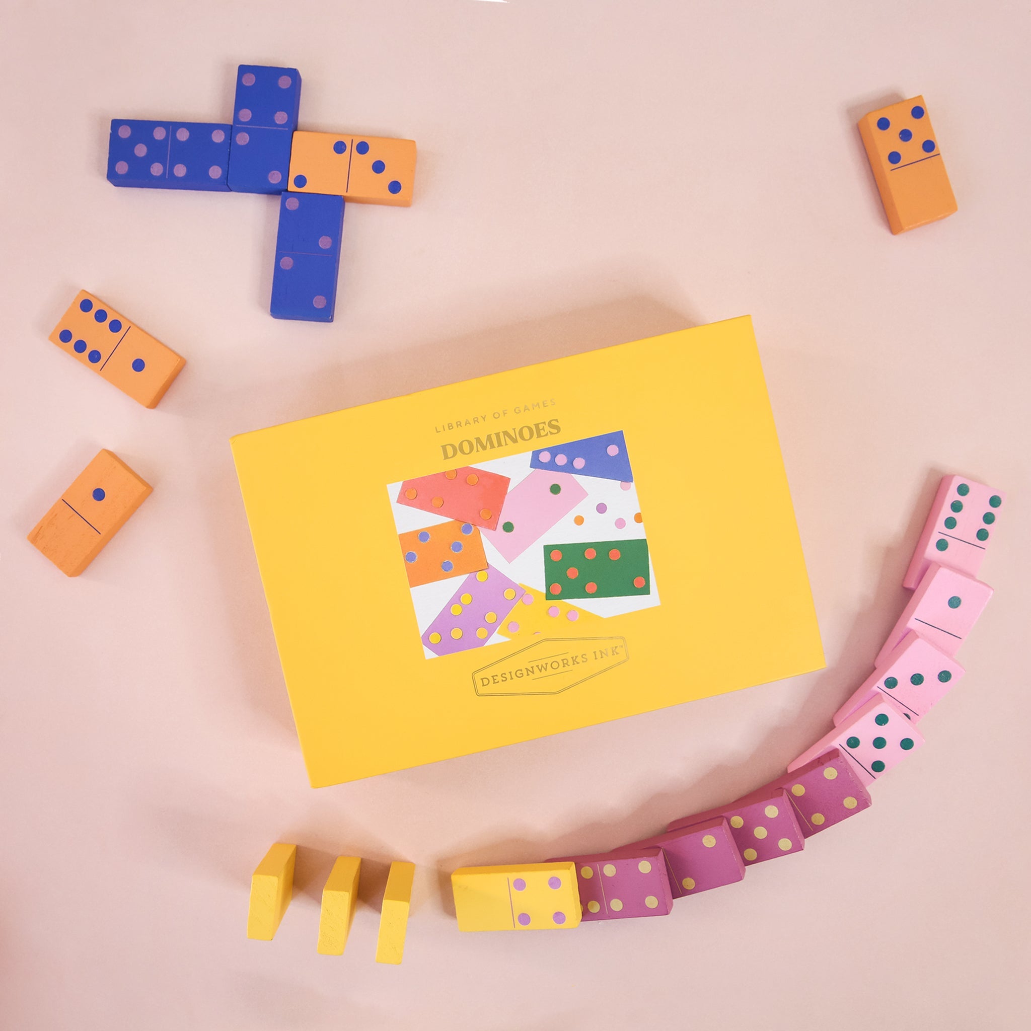 a colorful dominos set with a yellow box sits on a pink ground