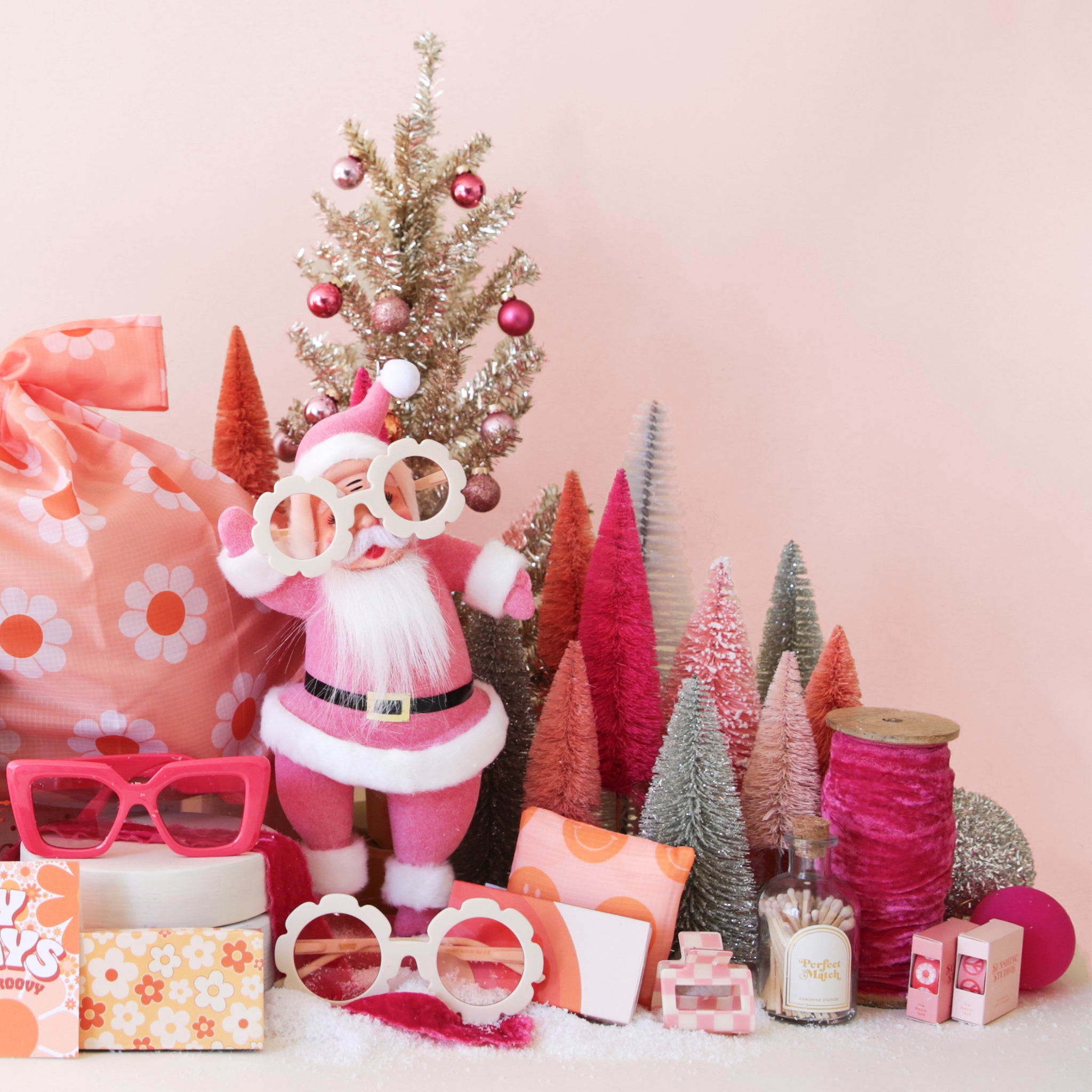 a collection of products featuring a pink santa figure wearing white flower shaped sunglasses, a pink and white floral bag, hot pink sunglasses, retro flower match box, colorful christmas trees, a glass match jar, and hot pink ribbon