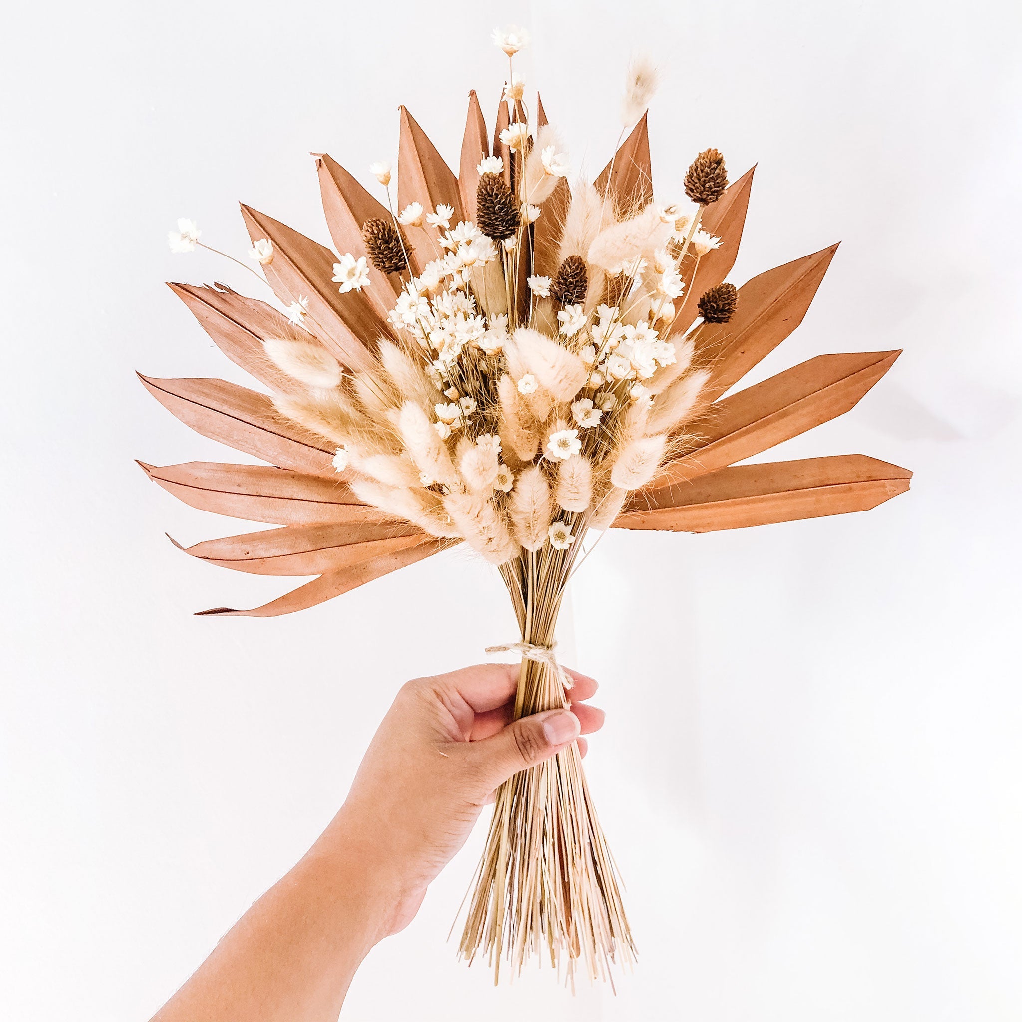 a hand holds a dried floral bouquet in a beige and brown color scheme