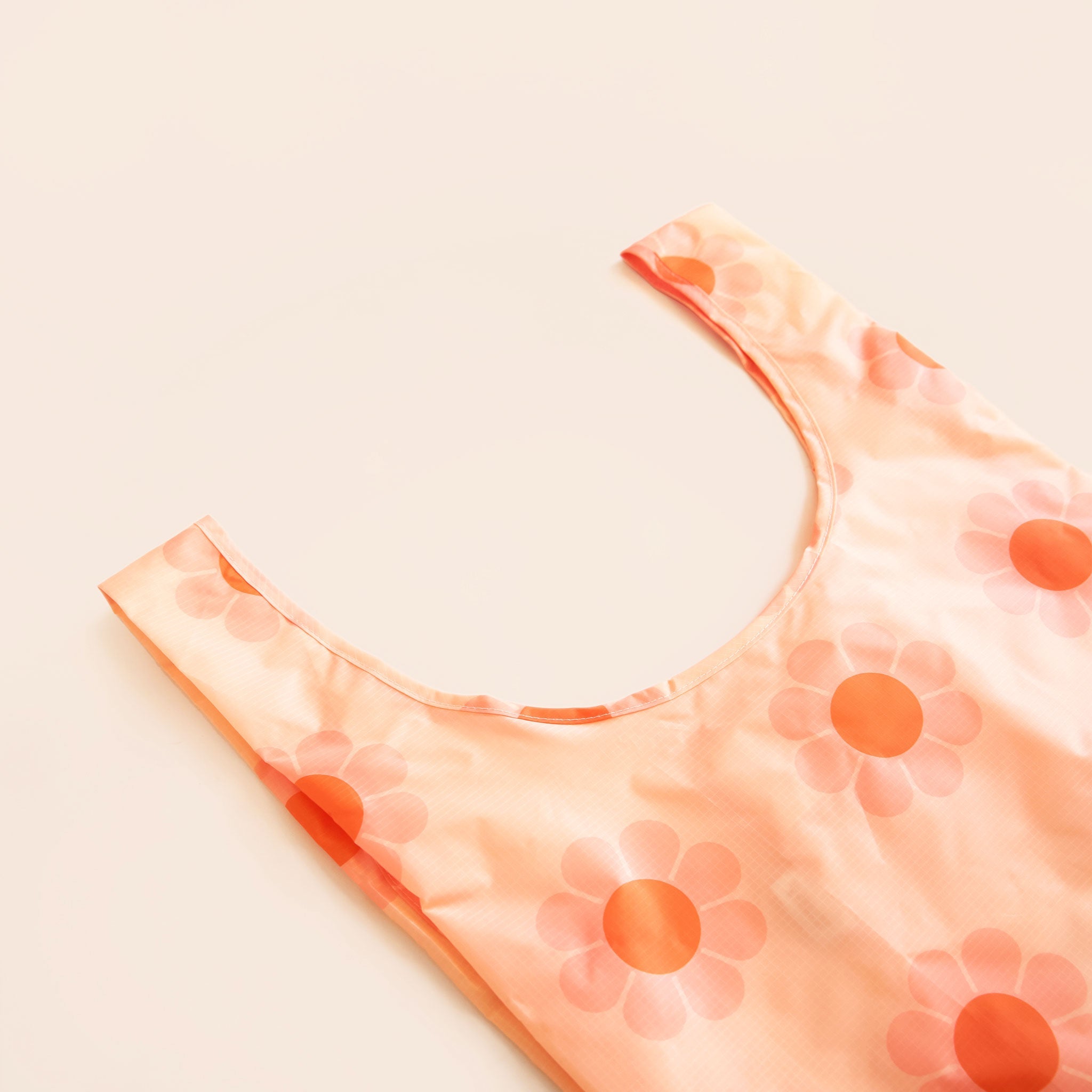 a peach colored tote bag with light pink and orange flower print sits on a light peach ground