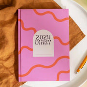 A pink and red squiggle diary with a white arch in the center and black text "2024 Diary".