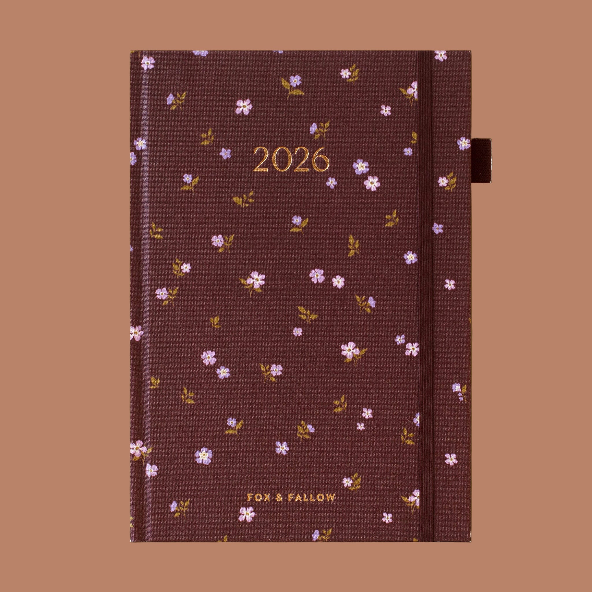 A dark maroon planner with gold foiled text that reads, "2026" with a floral print. 