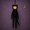 A black cat costume doll with a pale face and cat ears, hanging against a purple starry background with a gold crescent moon.