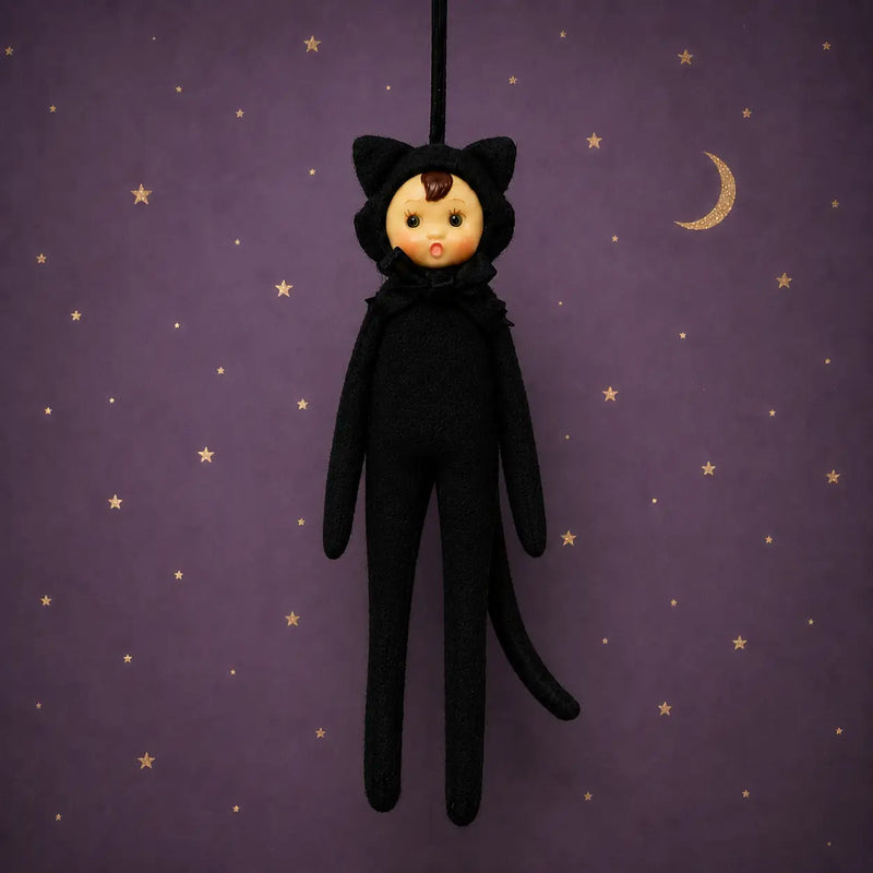 A black cat costume doll with a pale face and cat ears, hanging against a purple starry background with a gold crescent moon.