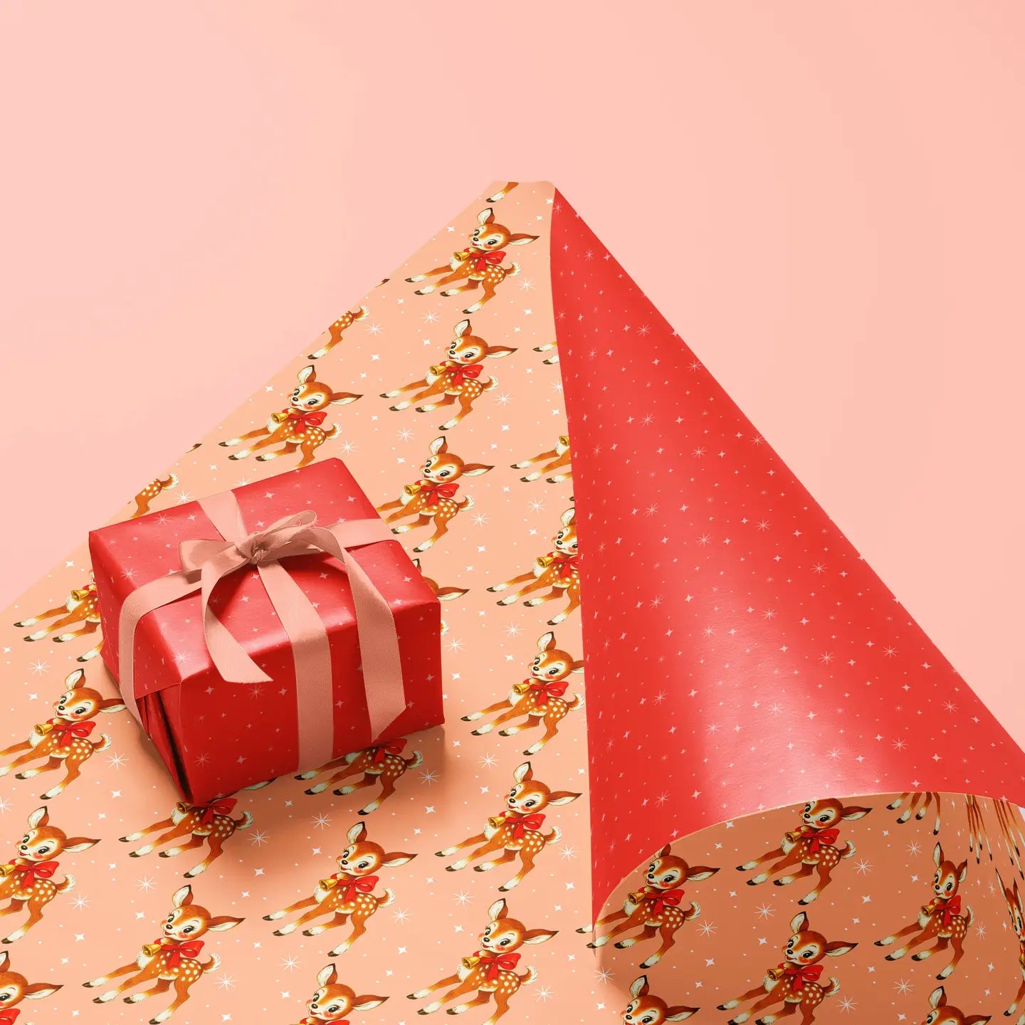 Holiday wrapping paper. One side is light orange with retro inspired deers and the other side is bright red with white stars. 