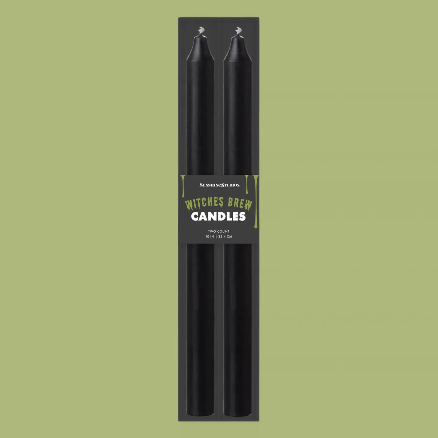 Two black taper candles in a tall black retail package with a label reading 'Witches Brew Candles' on a solid light olive-green background.