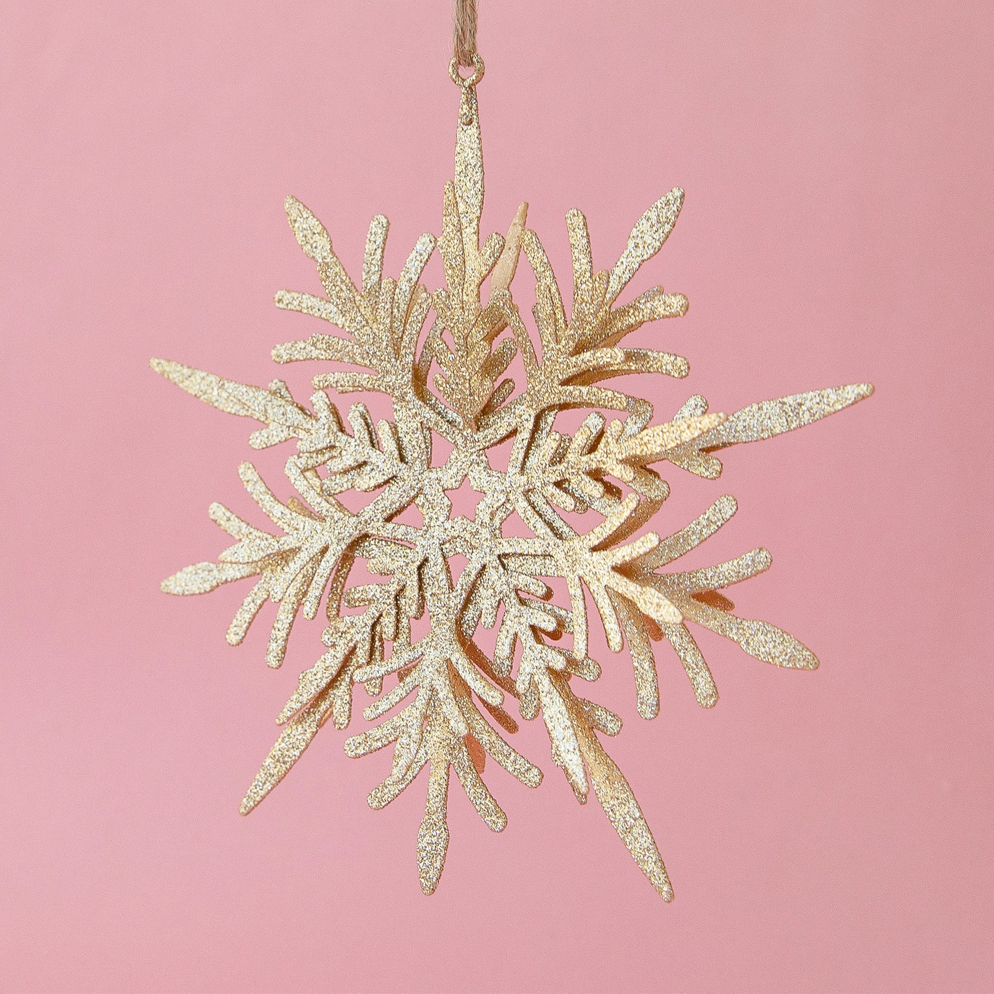 On a pink background is a gold glitter snowflake ornament.