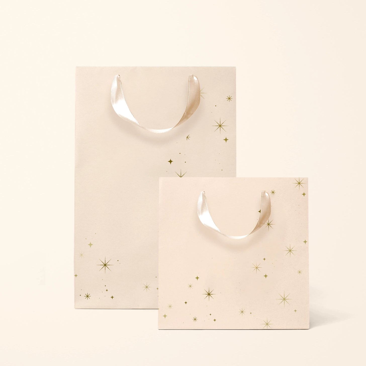 On an ivory background is two light pink gift bags with gold star details. 