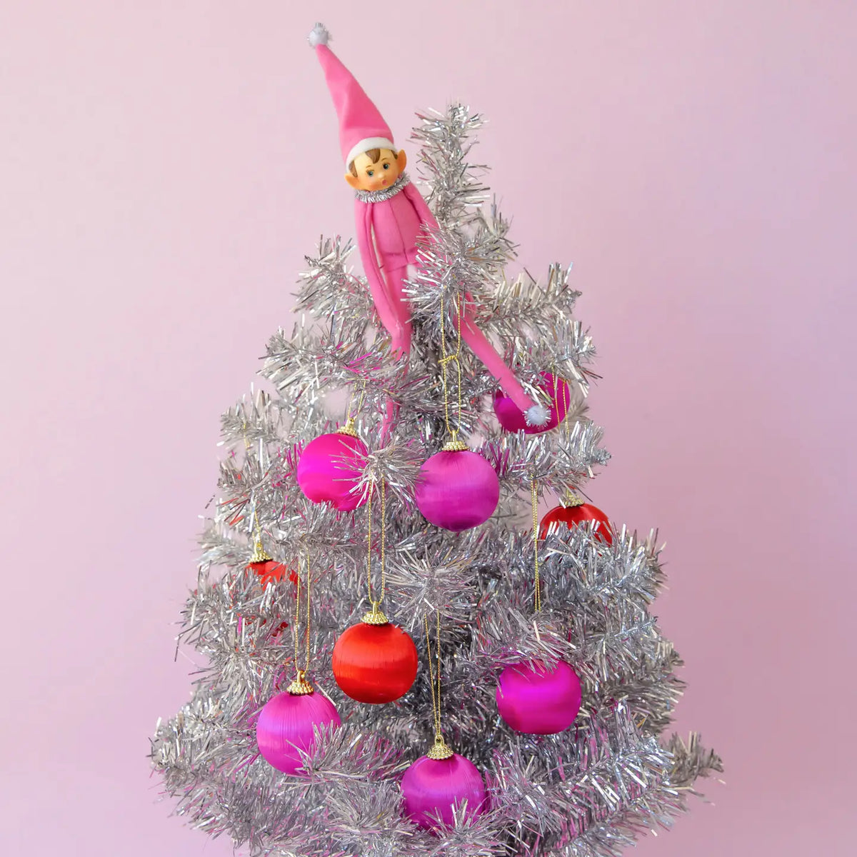 A silver tree adorned with the pink and red ornaments. 