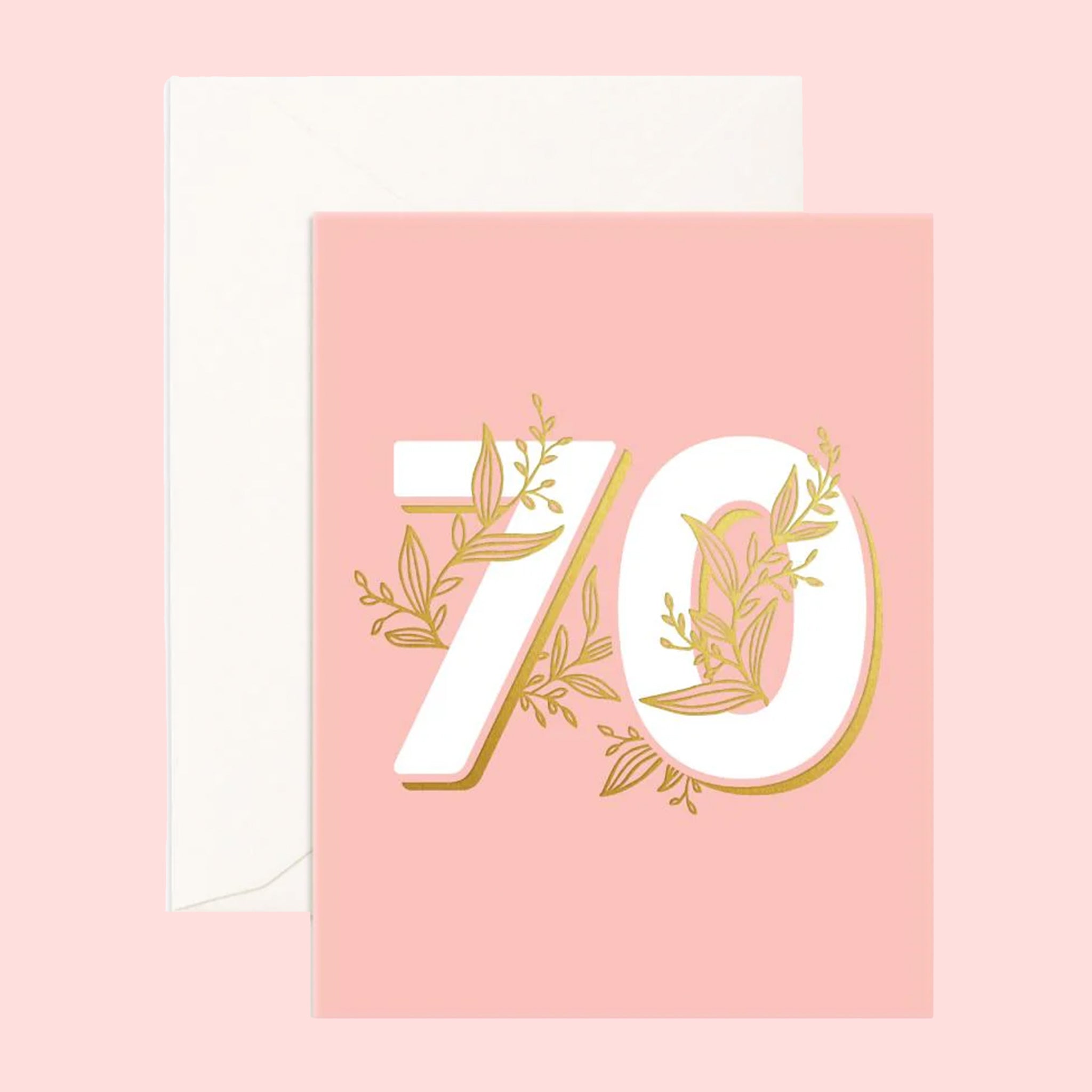 On a pink background is a pink greeting card with ivory "70" in the center with gold foiled details. 