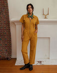 A dijon yellow utility suit with short sleeves, front pockets and a front zipper. 