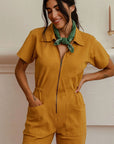 A dijon yellow utility suit with short sleeves, front pockets and a front zipper. 