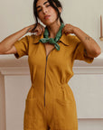 A dijon yellow utility suit with short sleeves, front pockets and a front zipper. 