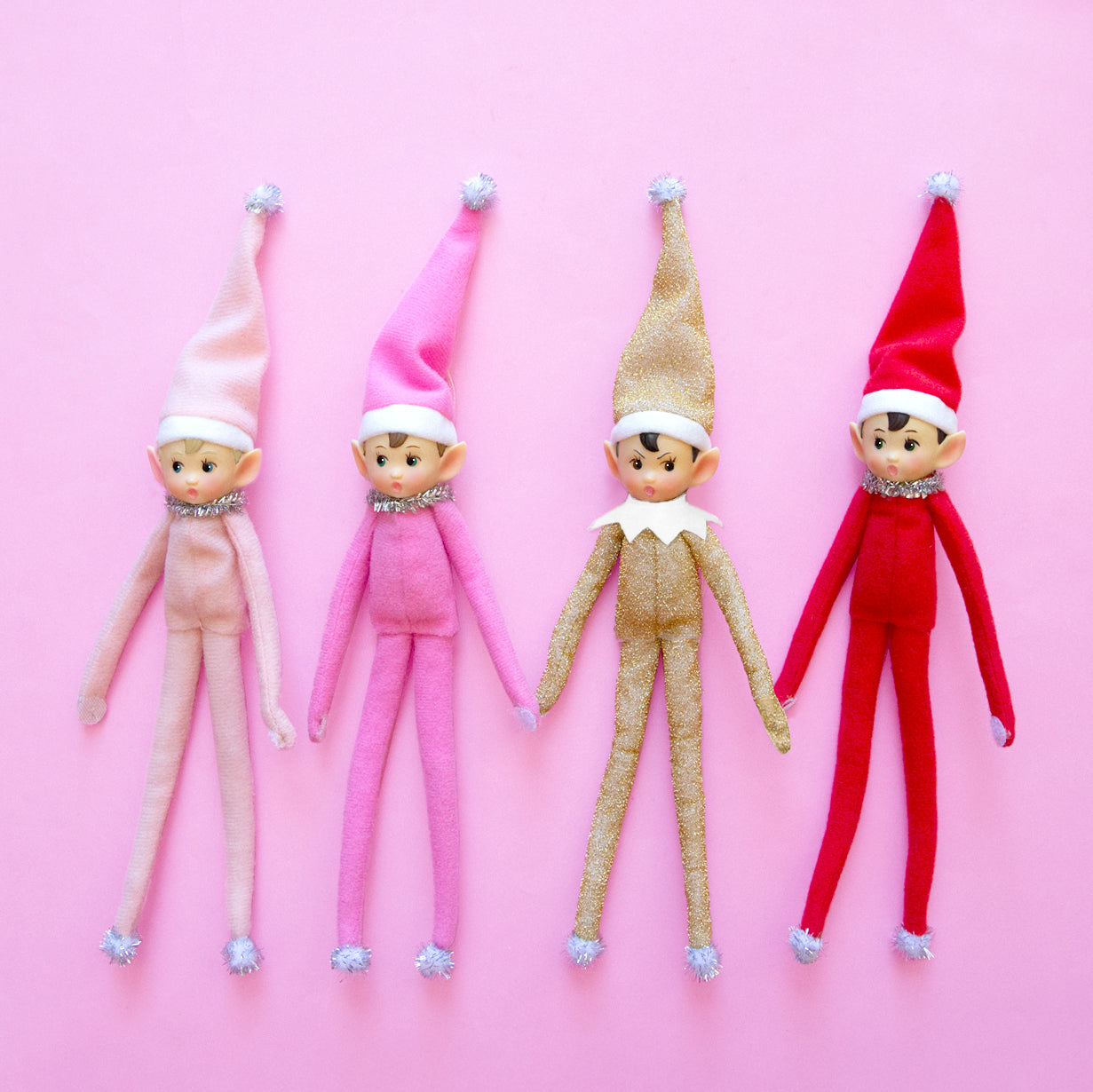 Four elf ornaments in light pink, dark ink, gold sparkle, and red. 