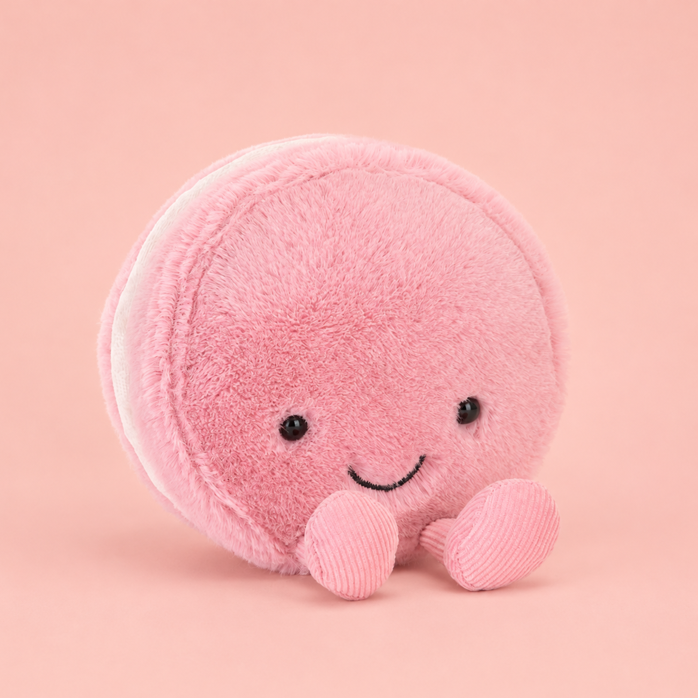 a pink maracon shaped plush toy with corduroy feet and a smiling face. 