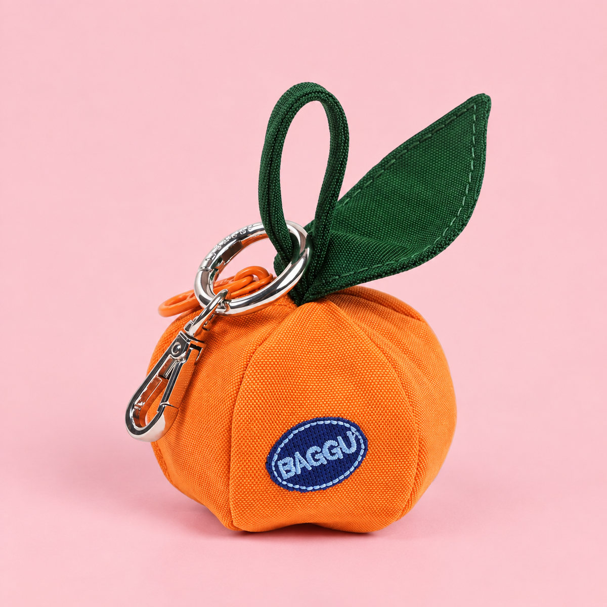 A round mandarin orange shaped bag charm that reads, "Baggu" embroidered on a blue patch. 