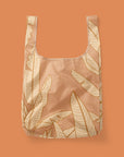 A light orange reusable nylon tote bag with a banana leaf pattern. 