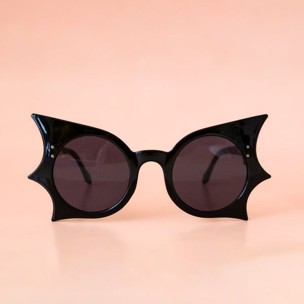 A black pair of sunglasses with a bat shape. 