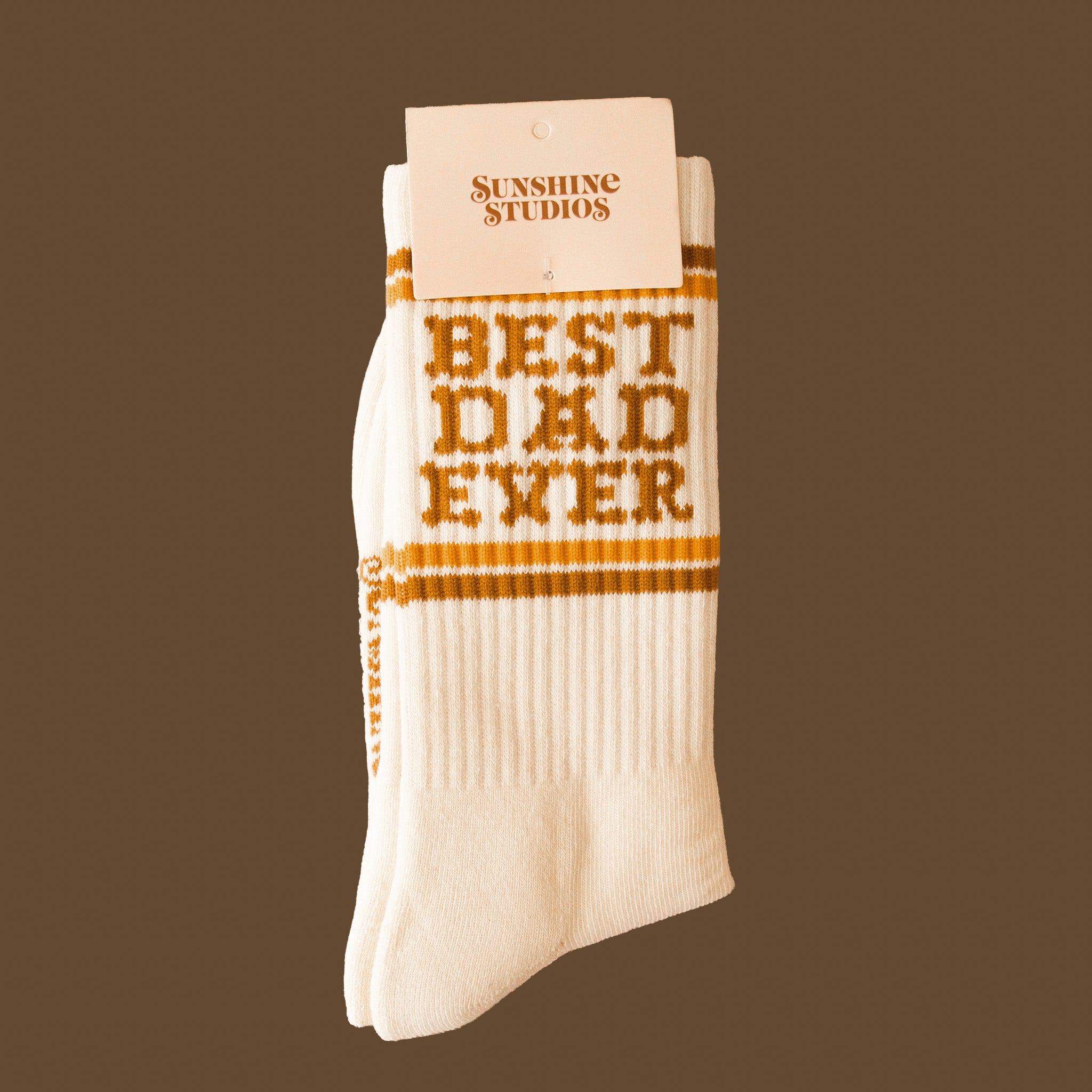 White crew tube socks with brown writing that reads "Best Dad Ever" and gold stripes on a brown background. 