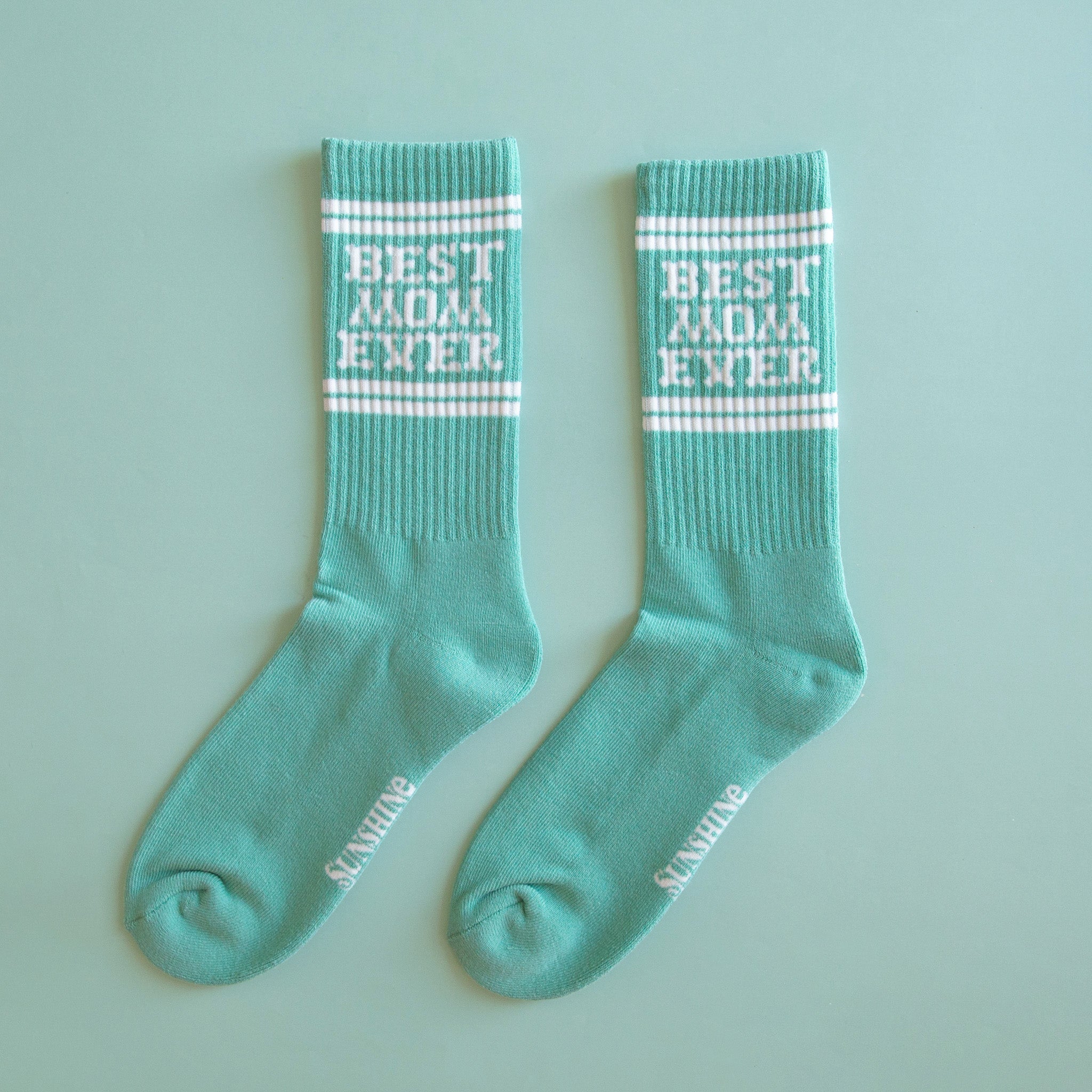 A turquoise pair of ribbed socks with white text and white stripes that reads, "Best mom Ever"