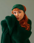 A red headed model wears a fuzzy emerald colored fur blanket with a green fur eye mask.
