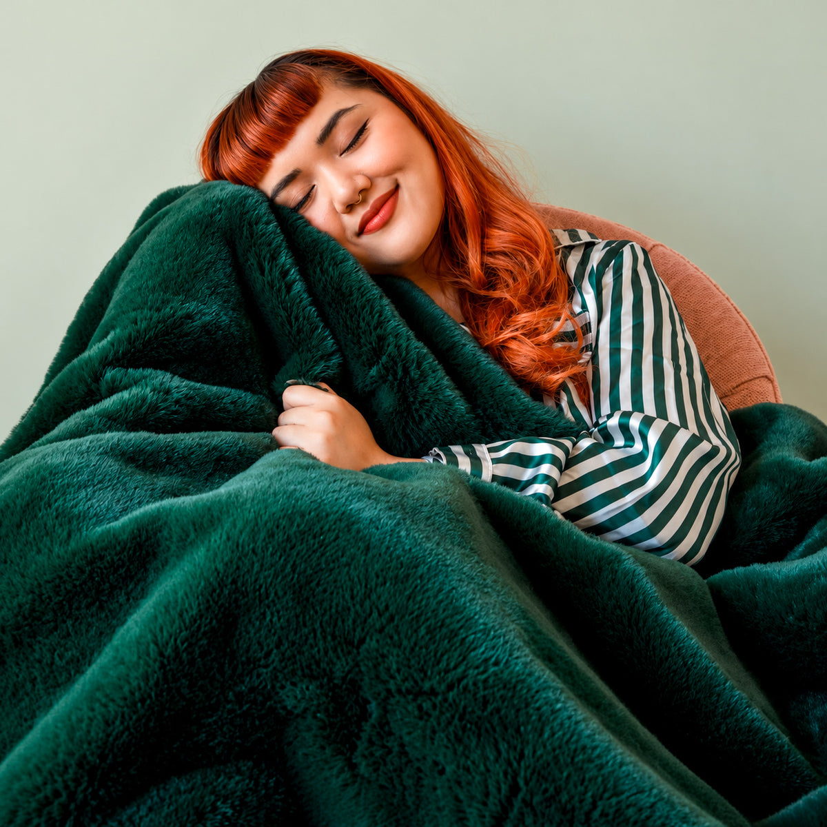 a model cuddling up in a green faux fur blanket. 