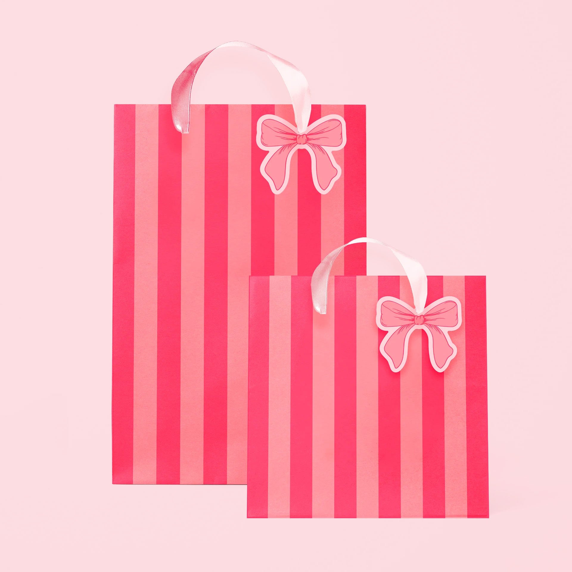 A light pink and hot pink striped gift bag in two different sizes with ribbon handles and a small bow shaped tag. 
