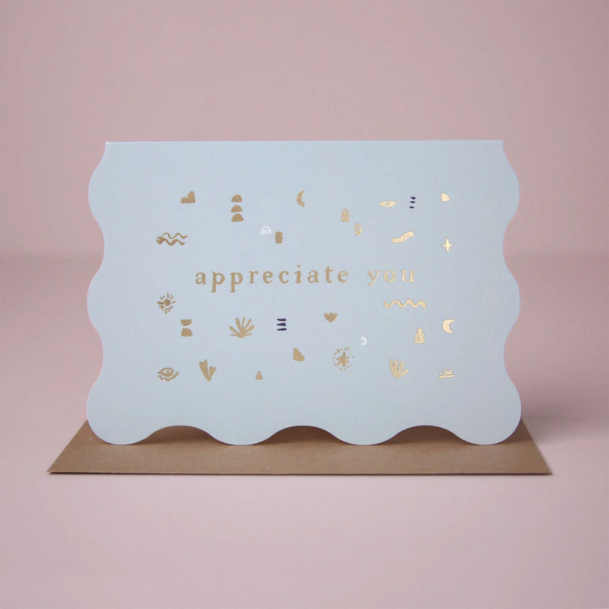 On a pink background is a light blue wavy card with gold foiled text that reads, &quot;appreciate you&quot;. 