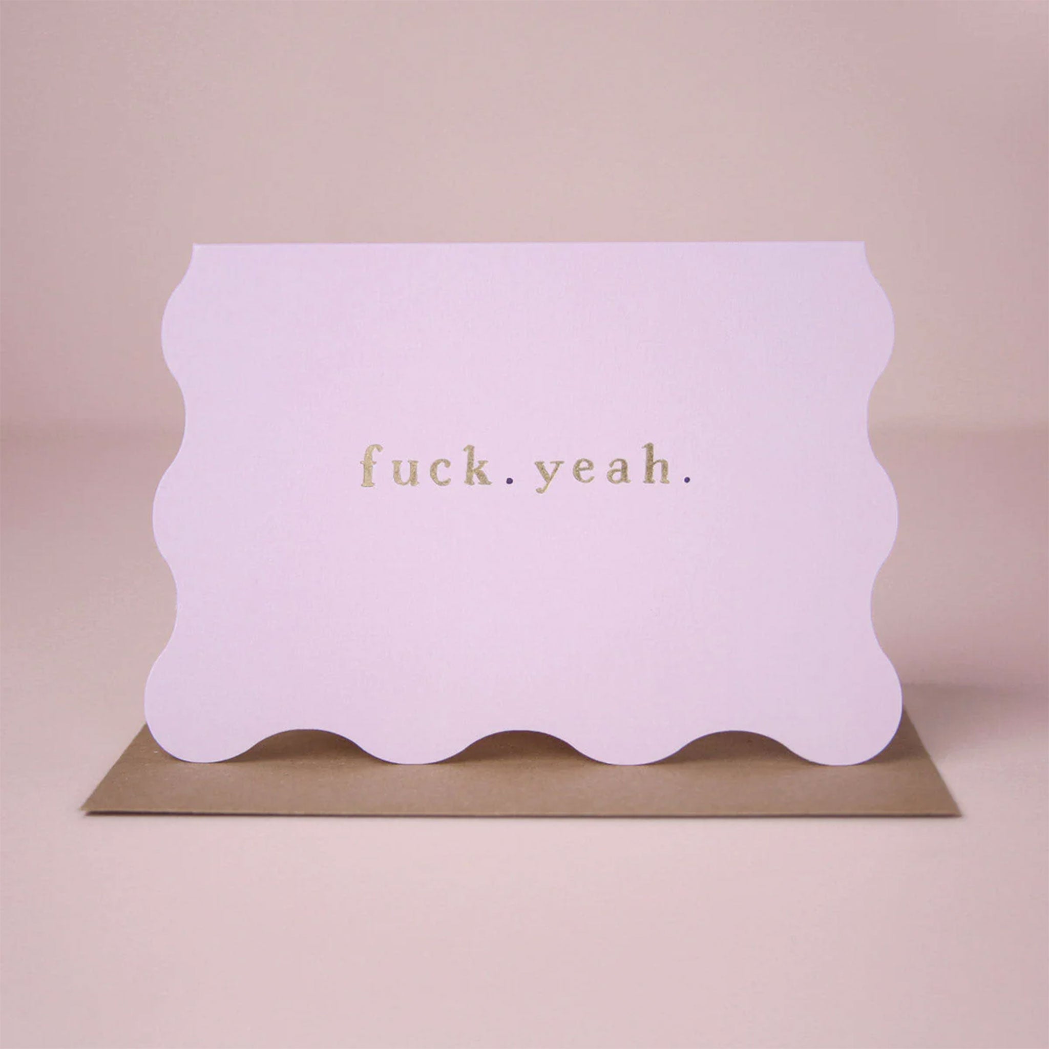 On a pink background is a wavy card with gold foiled text that reads, "fuck. yeah.". 