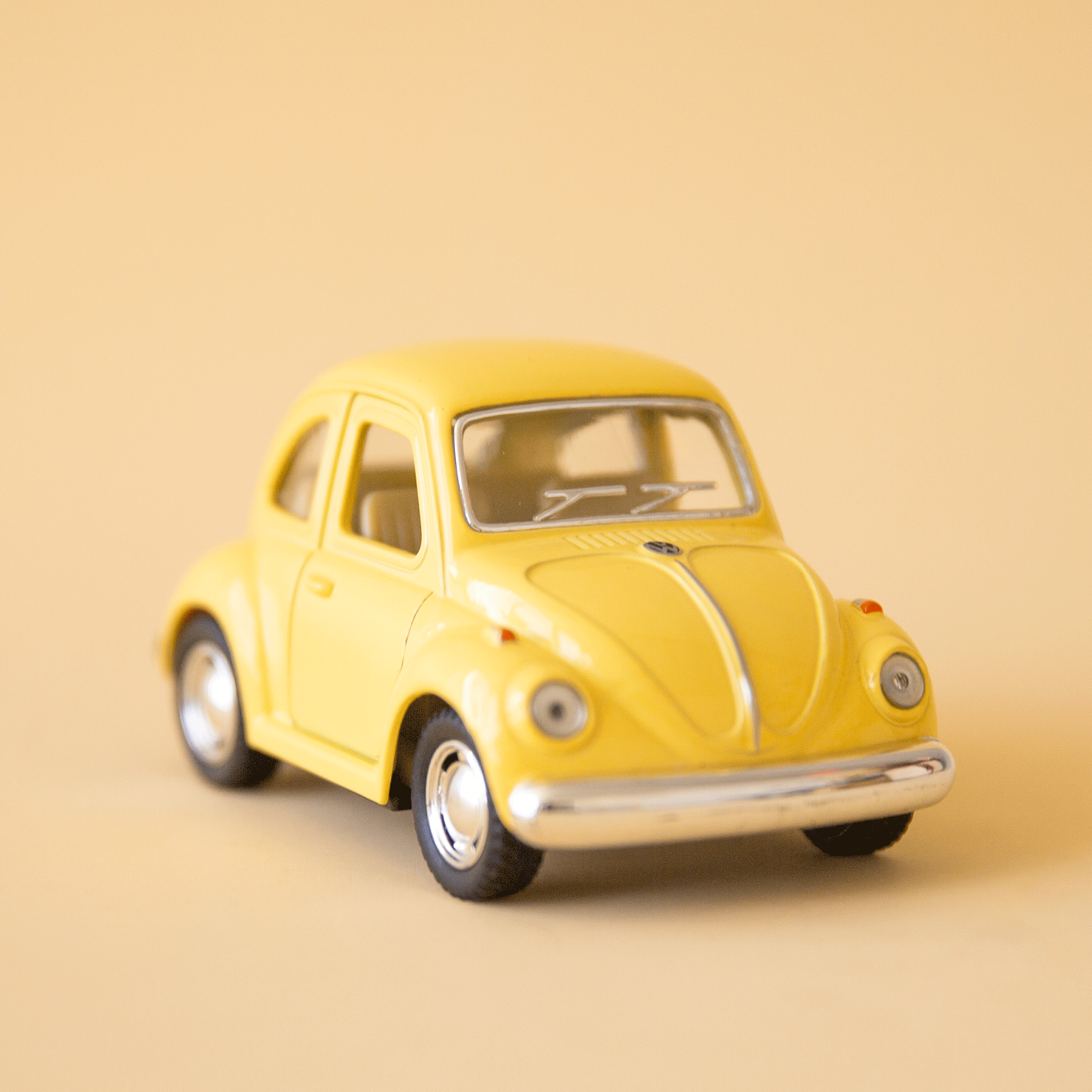 On a yellow background is a yellow vw beetle toy car. 