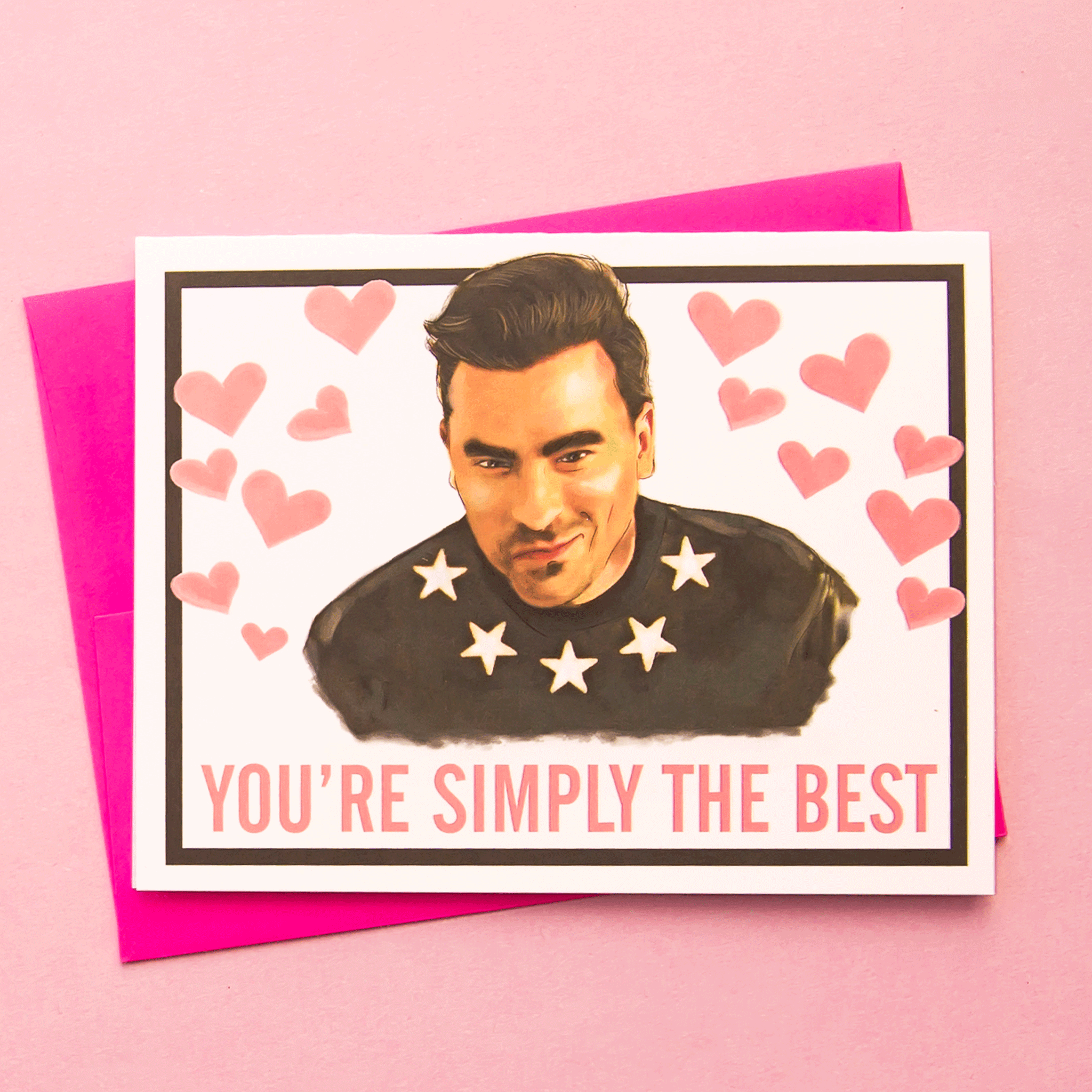 A white card with a black border and a graphic of David from Schitt&#39;s Creek along with 14 small pink hearts around him and pink text at the bottom that reads, &quot;You&#39;re Simply The Best&quot;. Also included is a pink envelope.