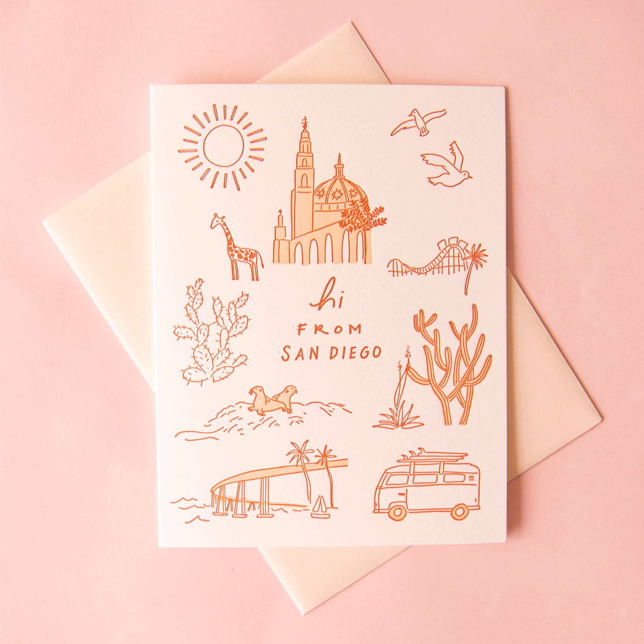 Photo of a greeting card that reads "hi from san diego" in rust letters on a white background. There are also rust colored simple line drawings of San Diego landmarks surrounding the writing, including a sun, the Coronado bridge, La Jolla beach seals, cacti, Balboa Park, and a giraffe representing the zoo.