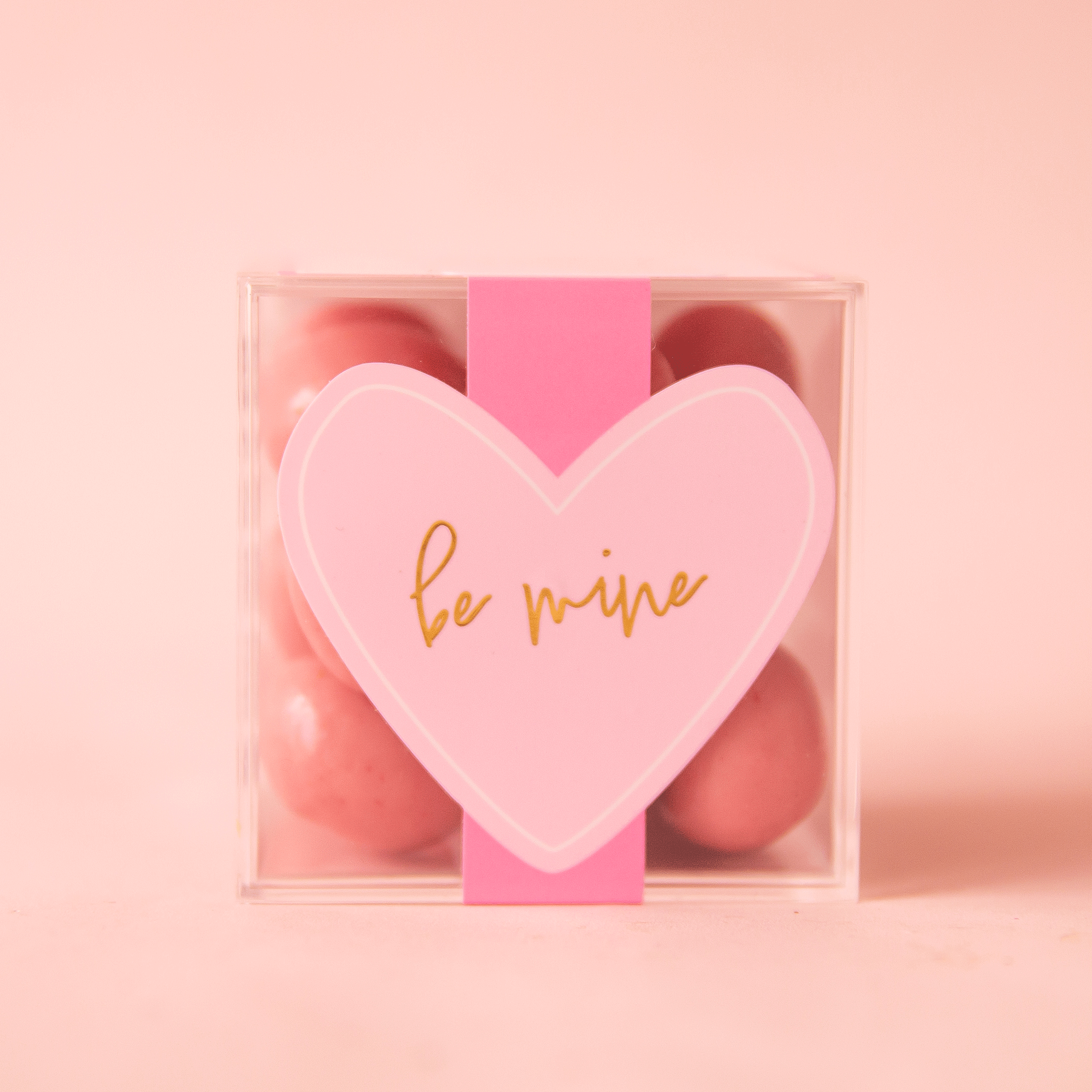 On a pink background is a clear acrylic box filled with pink shortcake cookie candies.