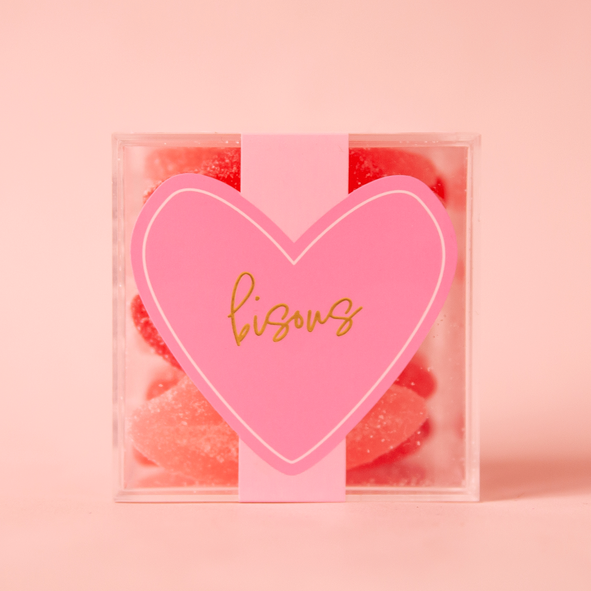 On a pink background is a clear acrylic box filled with sugar lips gummy candies.