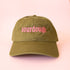An army green baseball cap with pink text that reads, 'sourdough'. 