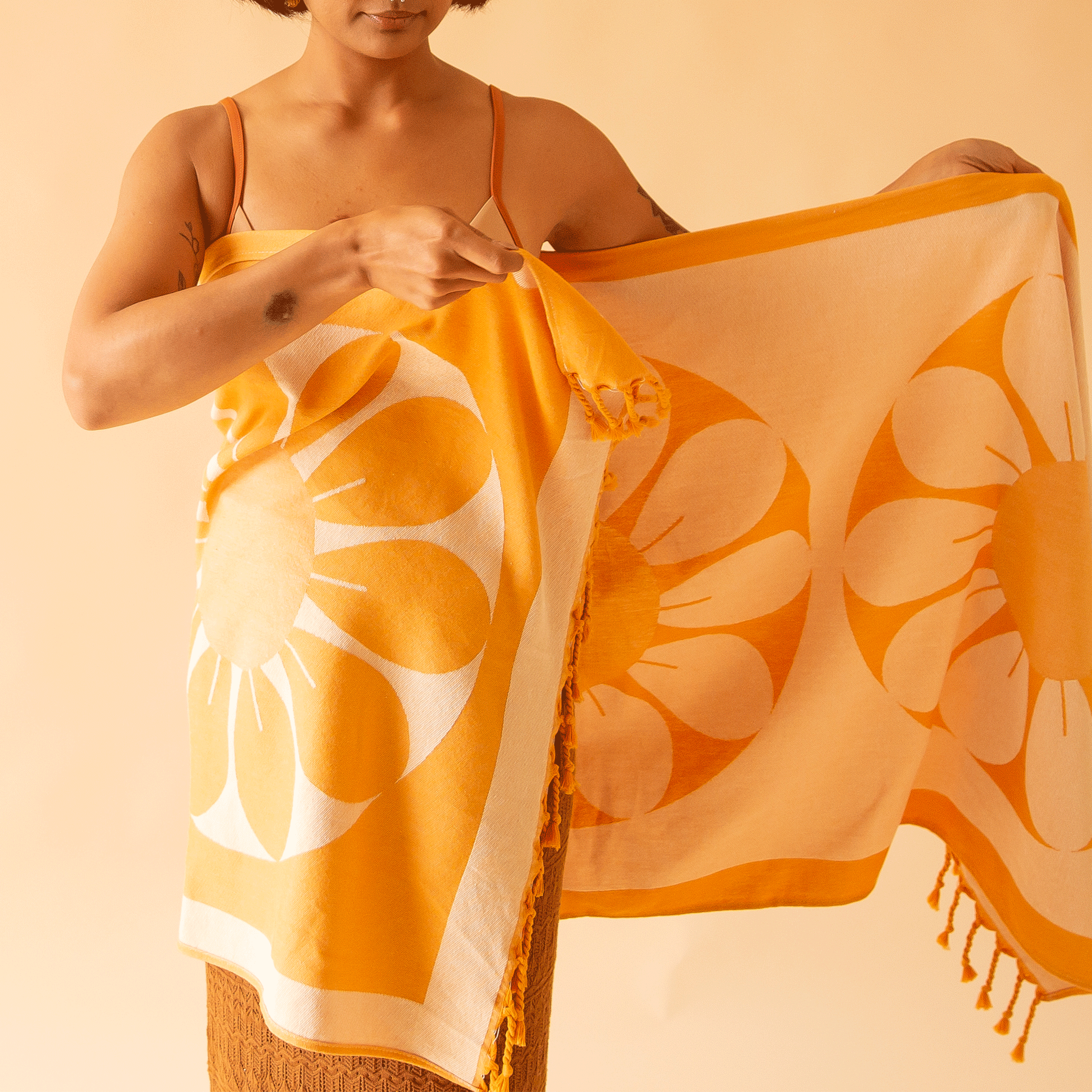 A model with the orange Retro Flower Beach Towel wrapped around their body. The towel has two large flower designs and orange tassels at both ends.