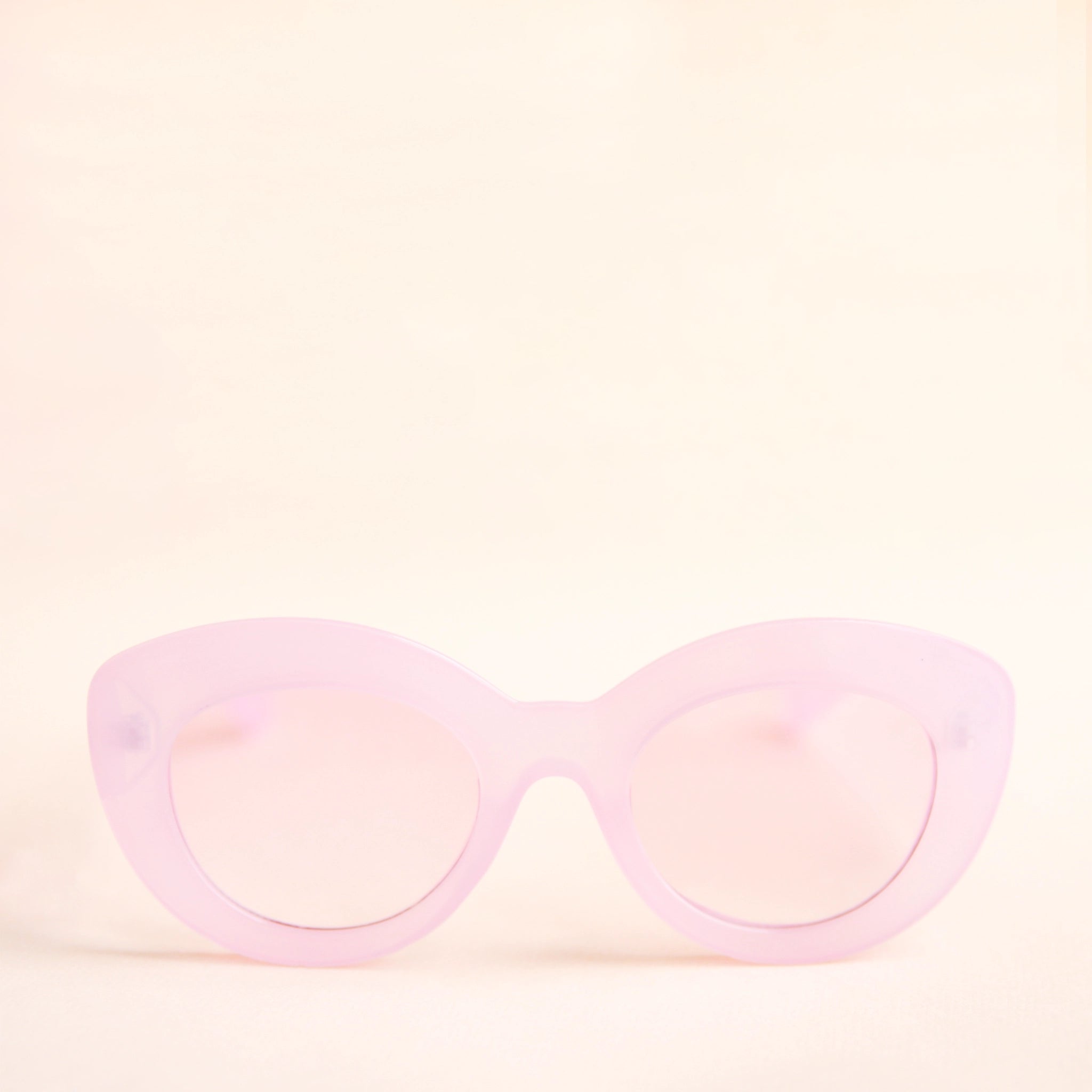 On a neutral background is the Gemma Sunglasses in the shade Amethyst. They have a rounded shape with a slight cateye flair at the corners. The frame material is a durable amber / peachy colored plastic and the lenses are a similar tone.