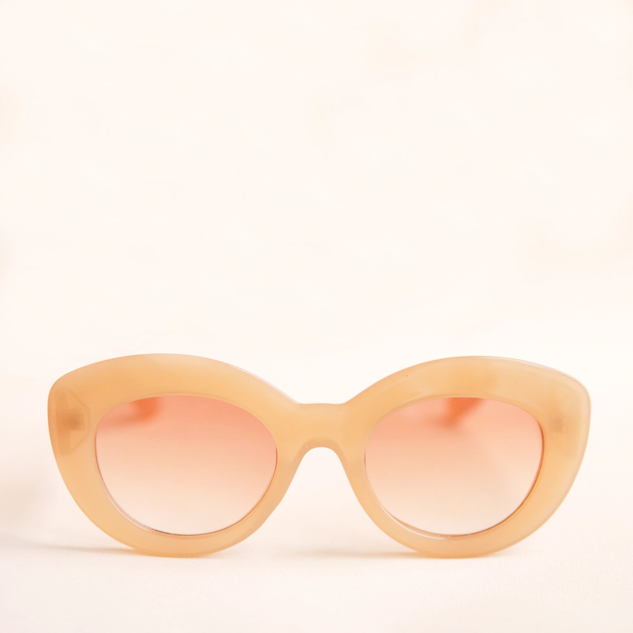 On a neutral background is the Gemma Sunglasses in the shade Amber. They have a rounded shape with a slight cateye flair at the corners. The frame material is a durable amber / peachy colored plastic and the lenses are a similar tone.