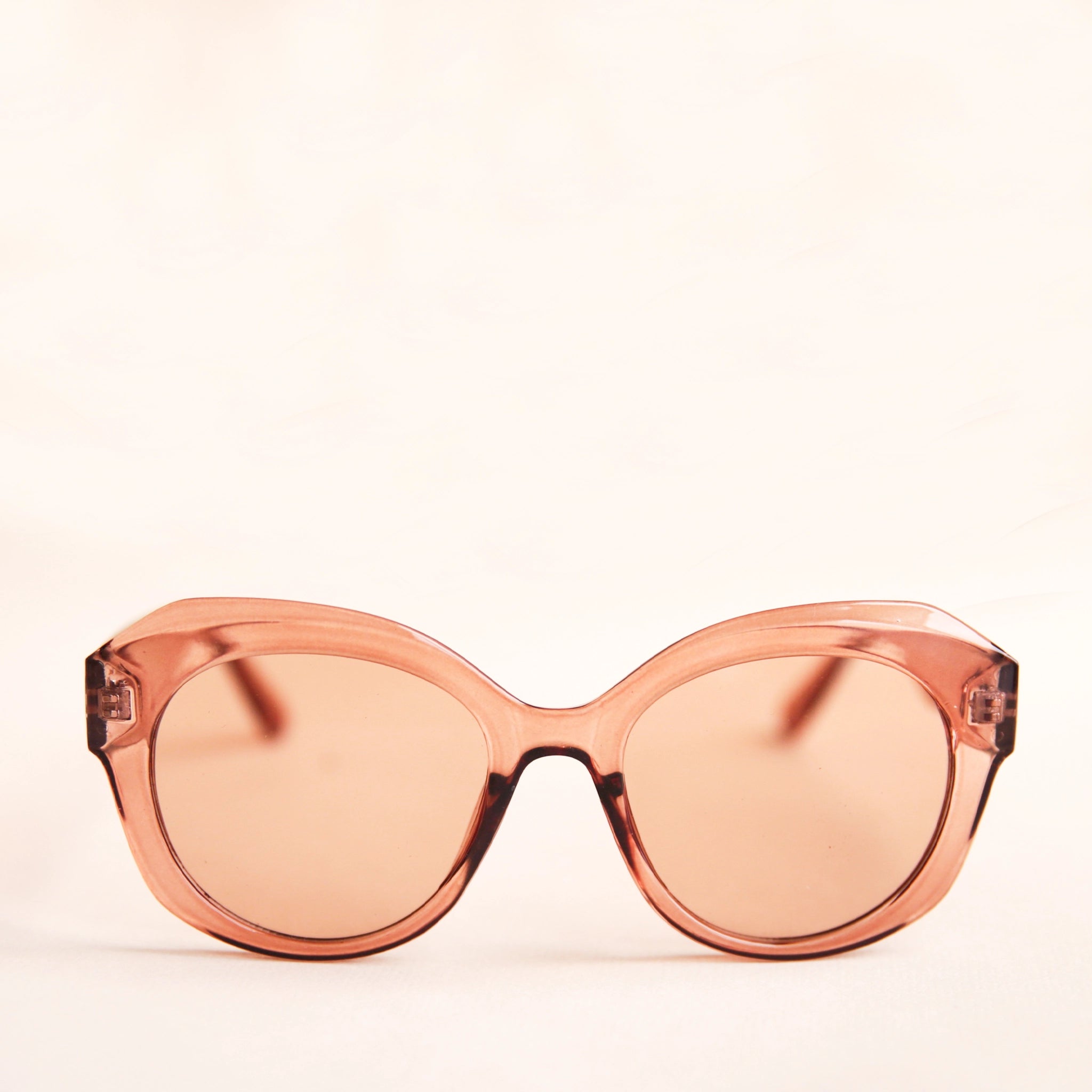 A light brown translucent pair of sunglasses that have a rounded shape and a light brown lens.