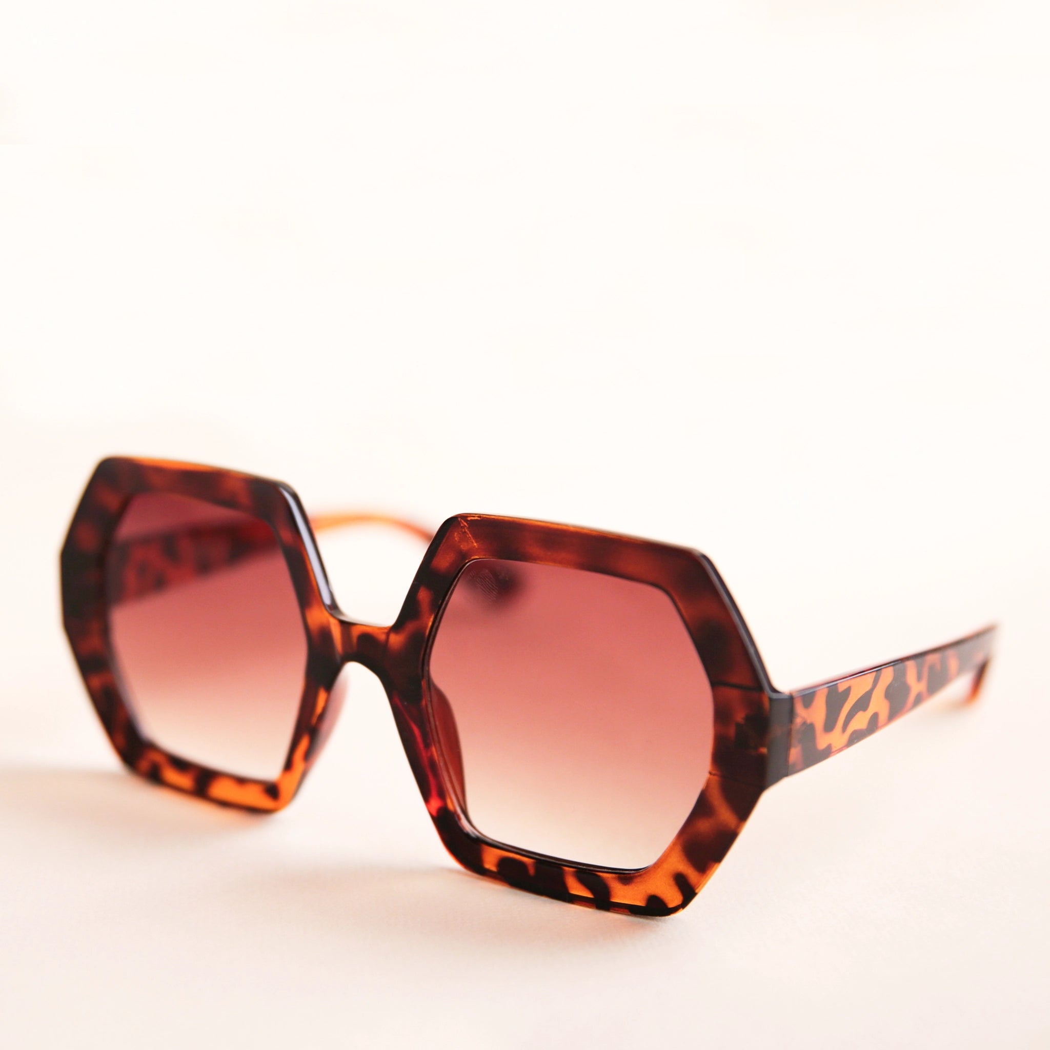 On a neutral background is a pair of hexagon shaped tortoise sunglasses with brown lenses.